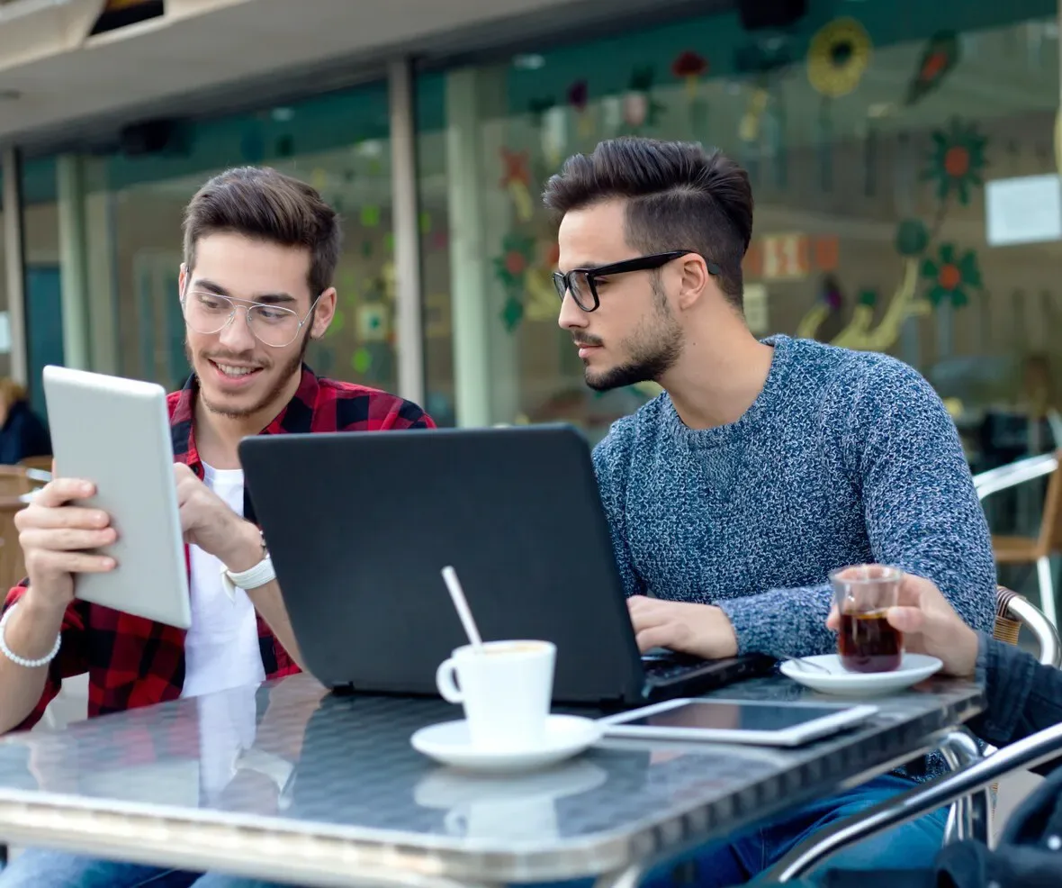 Two people working together over a laptop and tablet at a café
